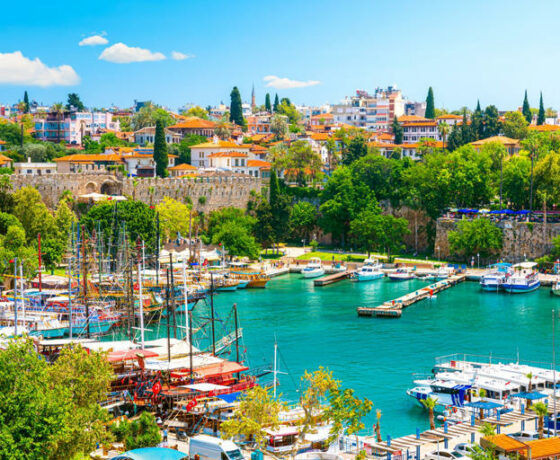 Vue panoramique d'Antalya en été avec plage, mer turquoise et montagnes en arrière-plan.